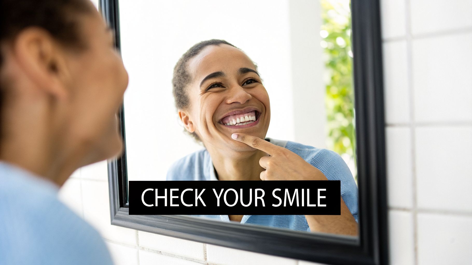 A happy person smiles and points at their teeth while looking in a mirror.