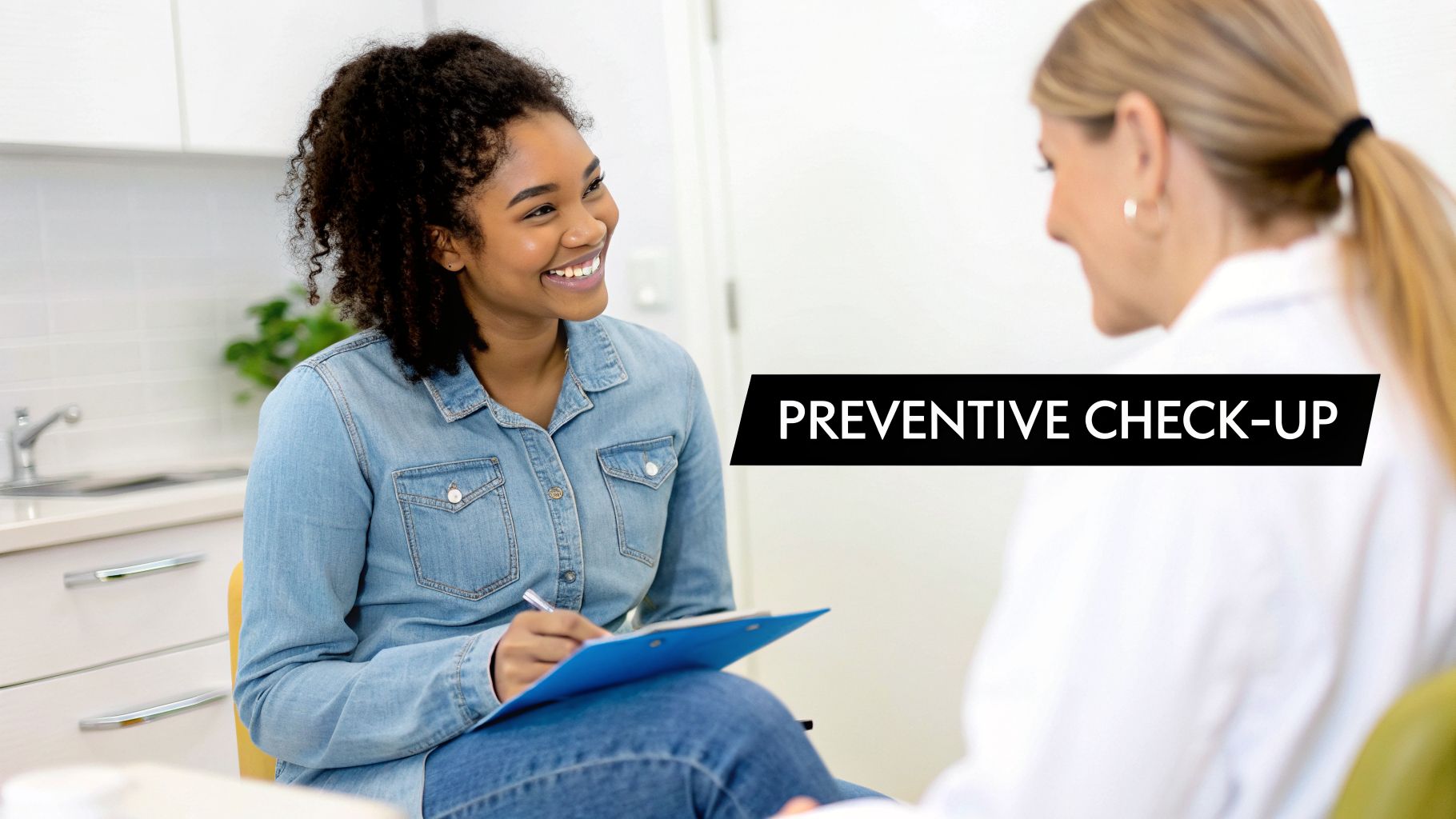 A smiling young Black woman in a denim shirt takes notes during a preventive check-up with a doctor.