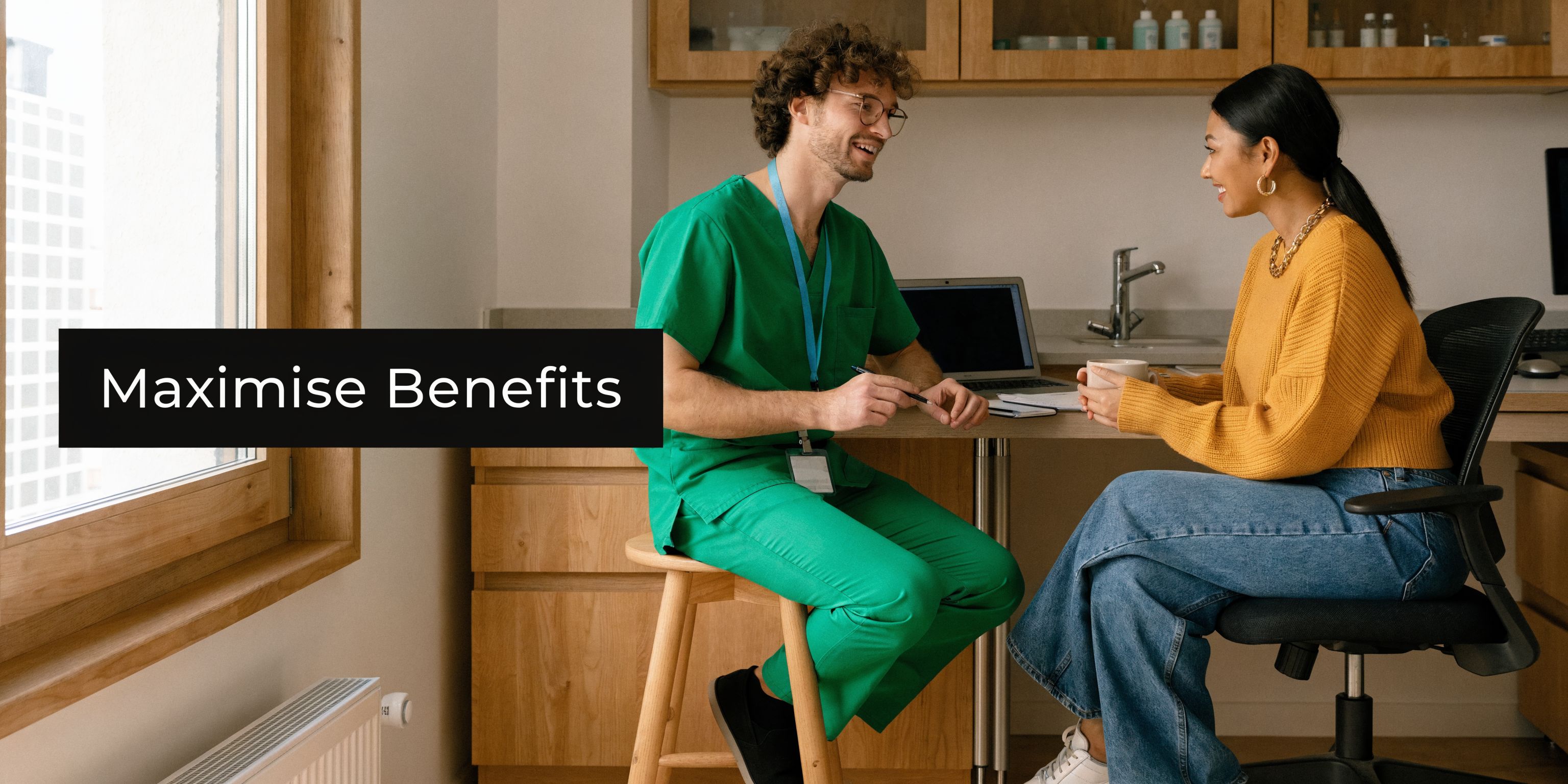 A male nurse in green scrubs converses with a female patient in a professional office setting.