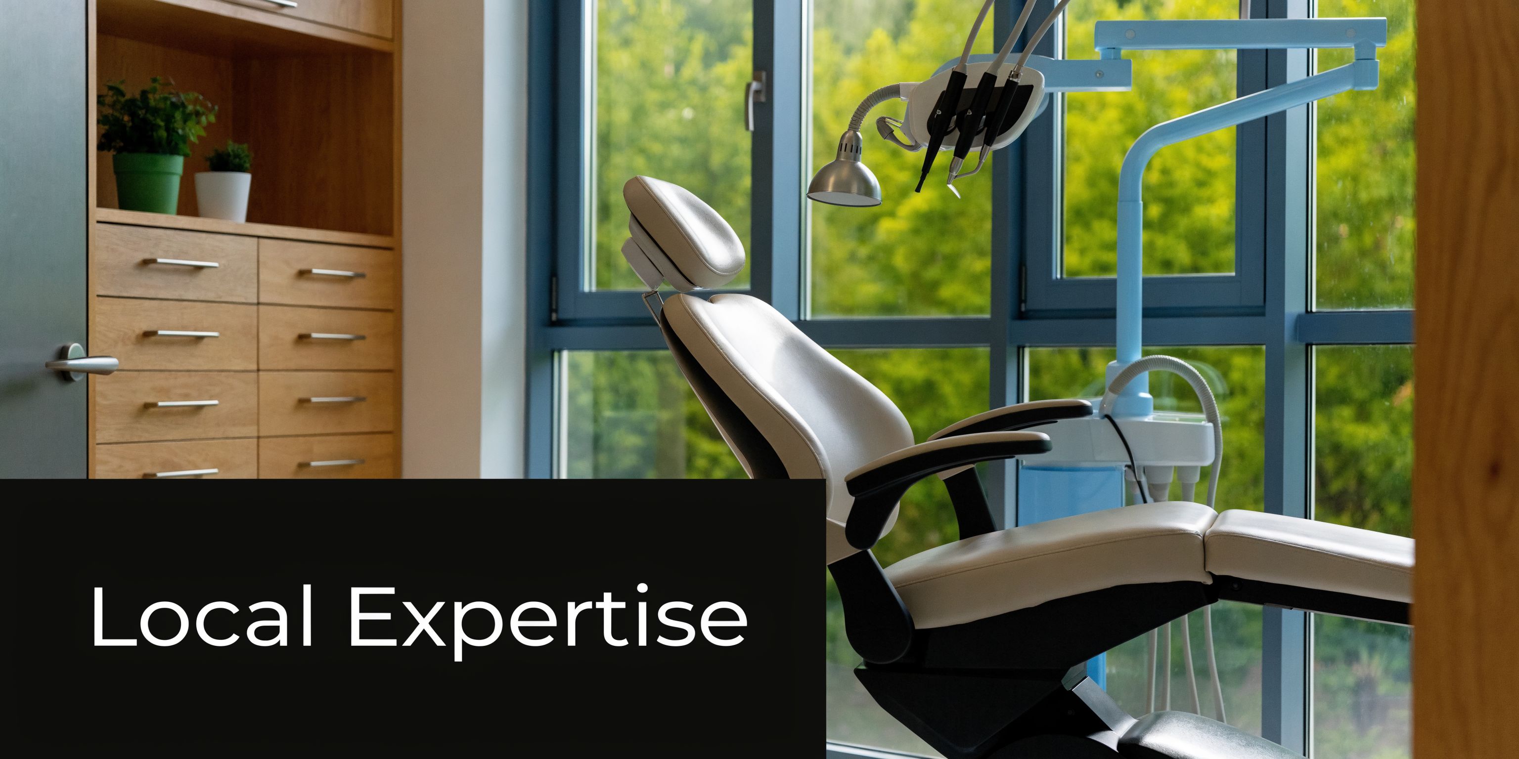 A clean and modern dentist office featuring a dental chair, medical equipment, and large windows with greenery.