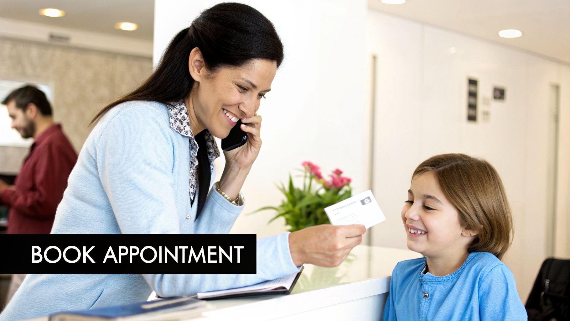 A smiling receptionist on the phone gives an appointment card to a happy child in a medical office.