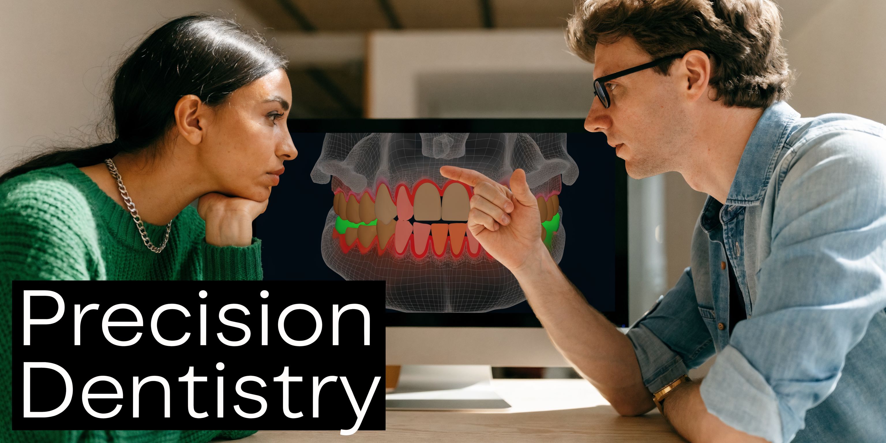 A dentist pointing at a computer screen showing a 3D dental scan to a female patient.