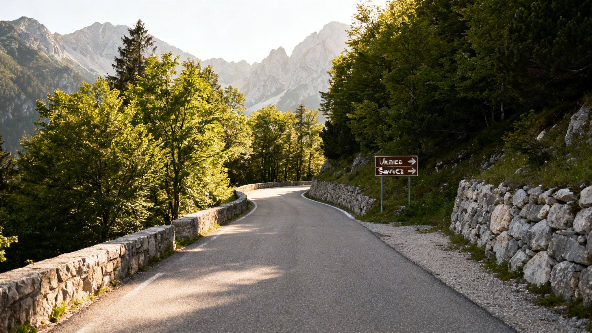 A winding mountain road through lush green trees with a sign directing to Ukanc and Savica.