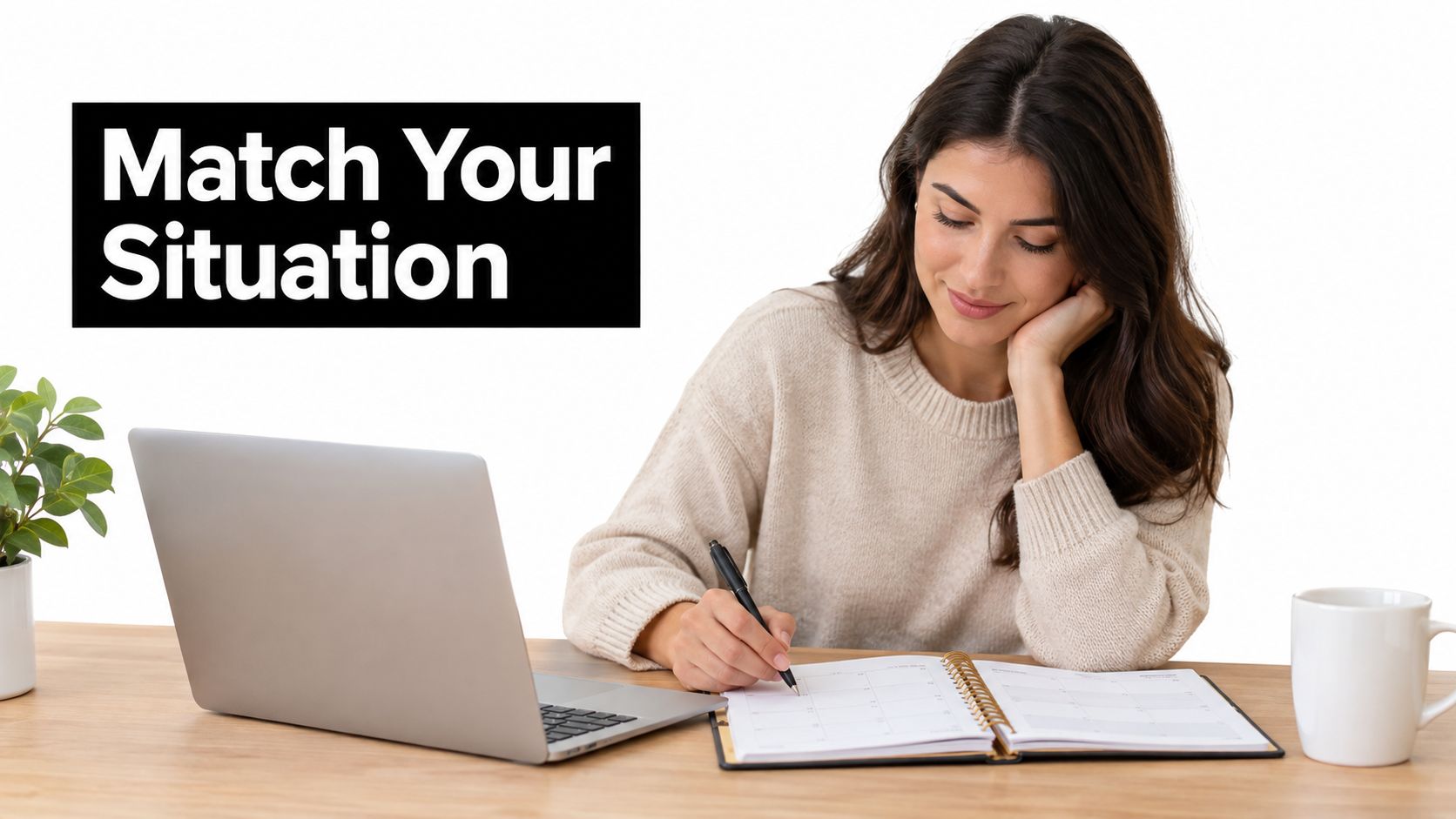 A smiling woman sitting at a desk writing in a planner with a laptop nearby.