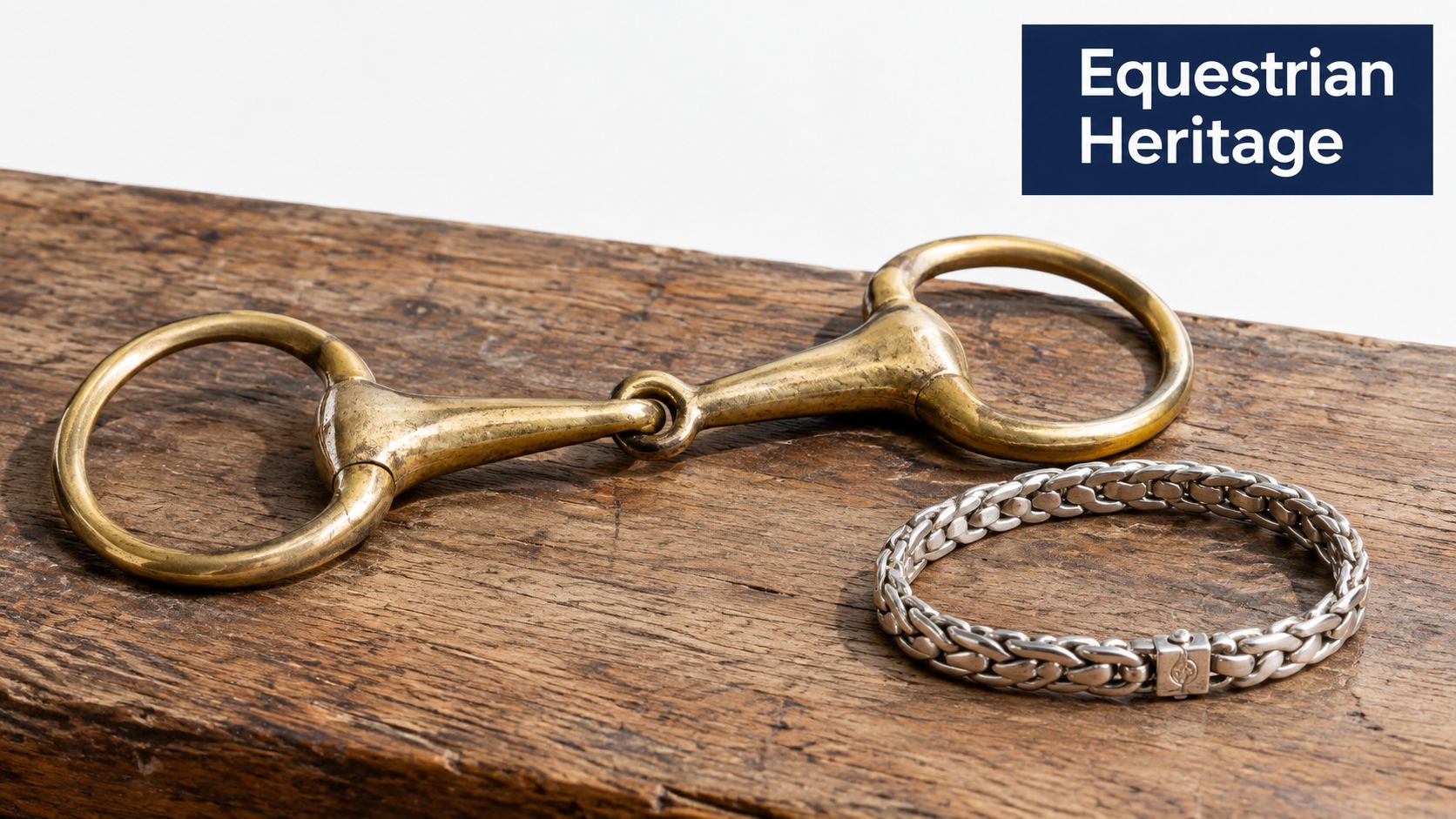 A brass horse bit lying on a rustic wooden board next to a sterling silver chain bracelet.