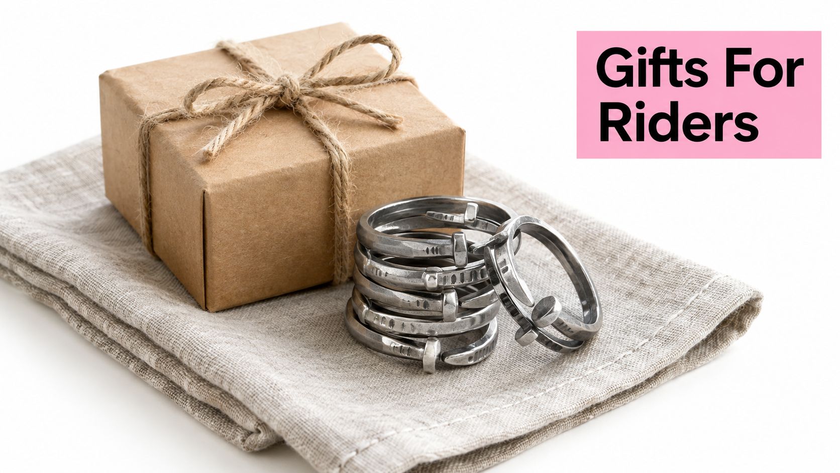 A stack of silver horseshoe nail rings sitting on a linen cloth next to a gift box.