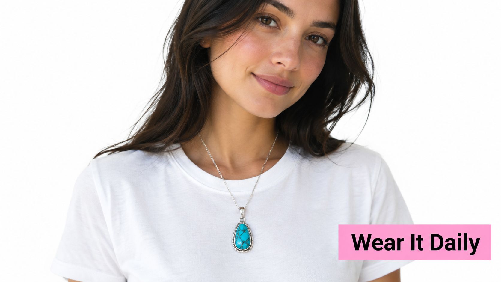 A smiling woman wears an elegant, teardrop-shaped turquoise and sterling silver pendant necklace with a white t-shirt.
