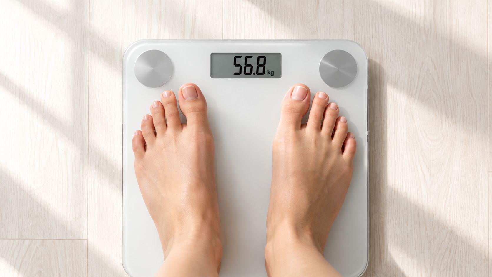 A person standing on a white digital bathroom scale on a wooden floor displaying their weight.