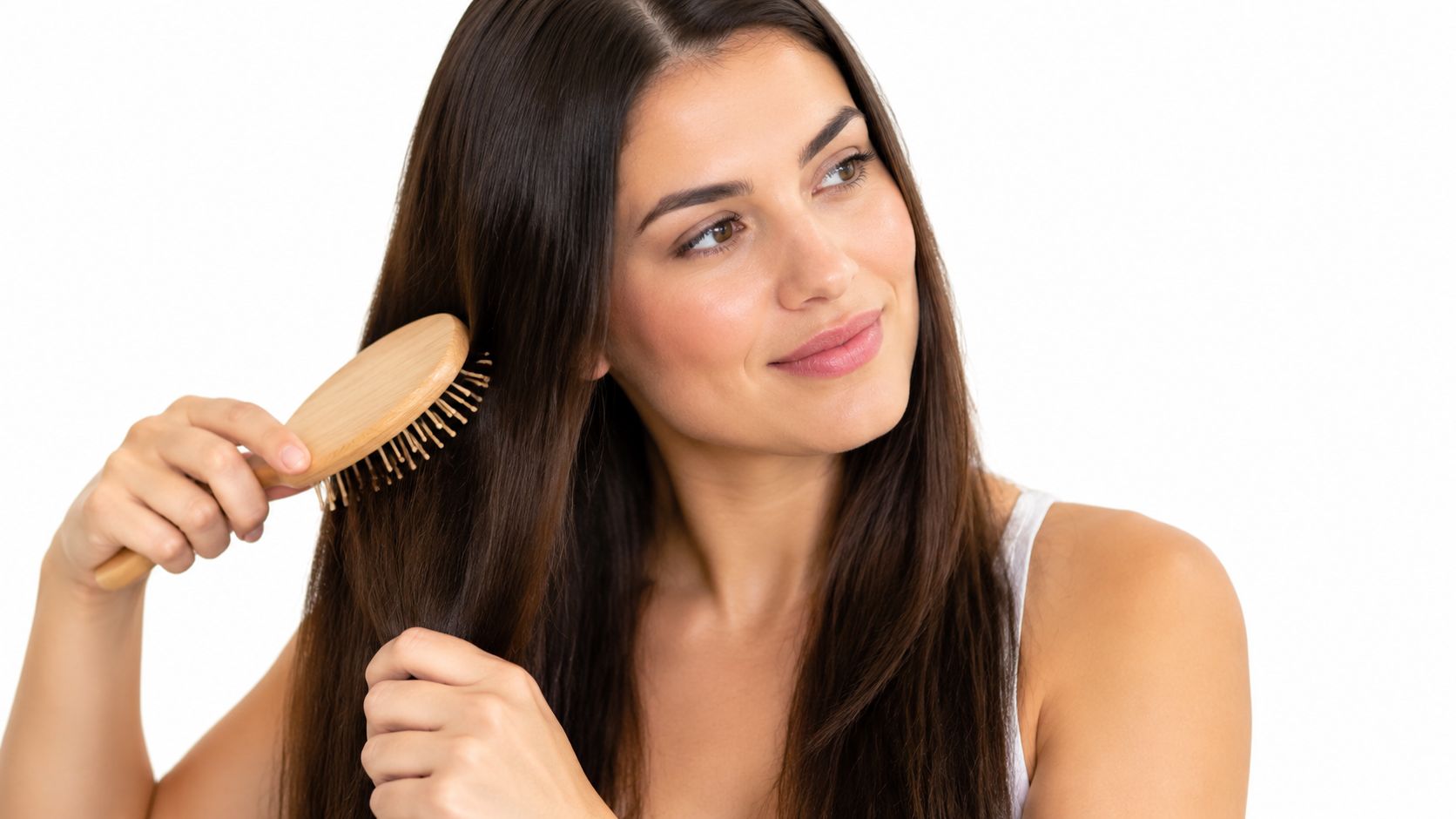 A smiling woman with long brown hair brushing her hair with a wooden hairbrush