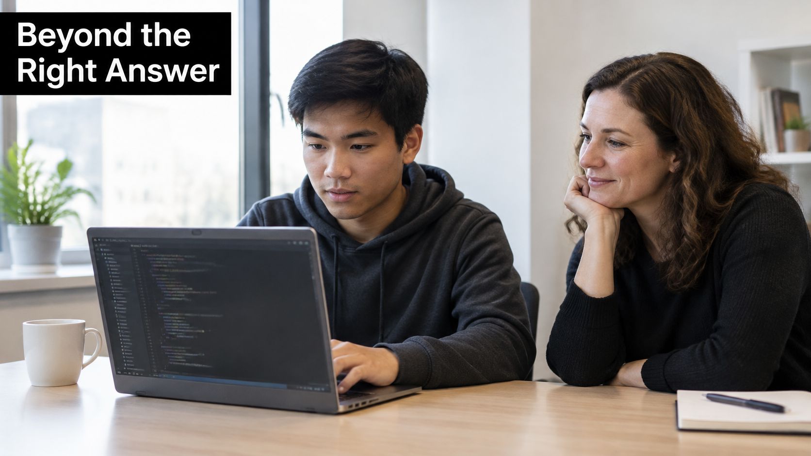 A young man coding on a laptop while a woman mentor observes and guides him closely.