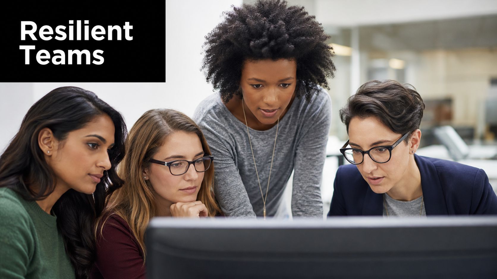 A diverse group of four female colleagues working collaboratively on a computer monitor in an office.