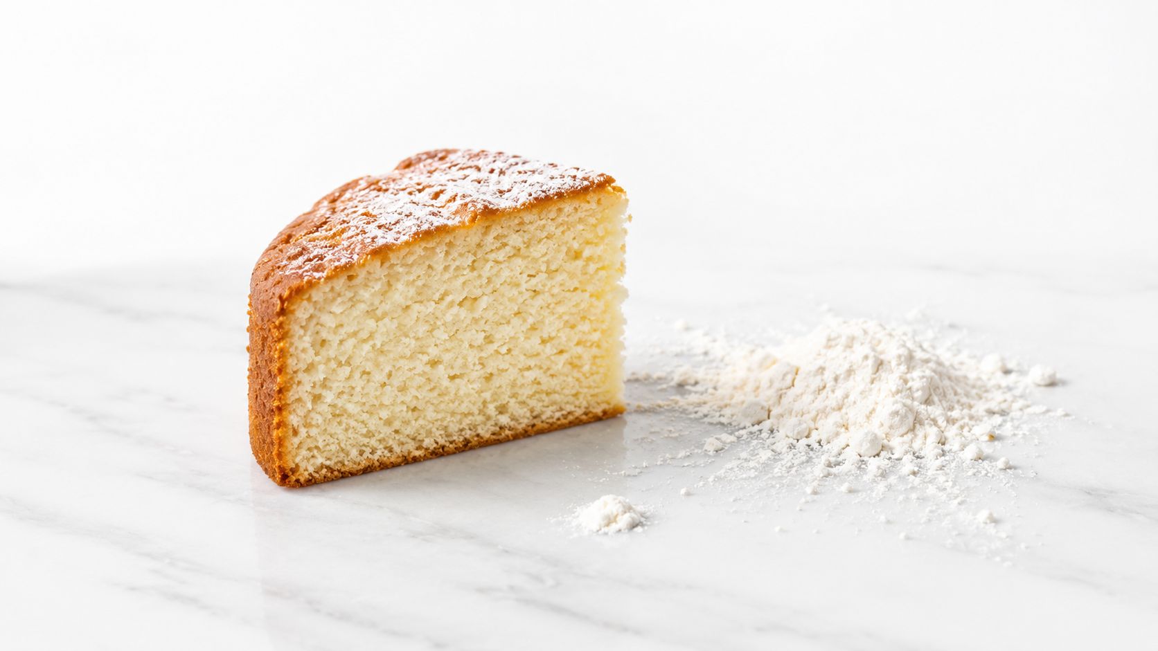 A slice of plain sponge cake dusted with powdered sugar next to a small pile of flour.