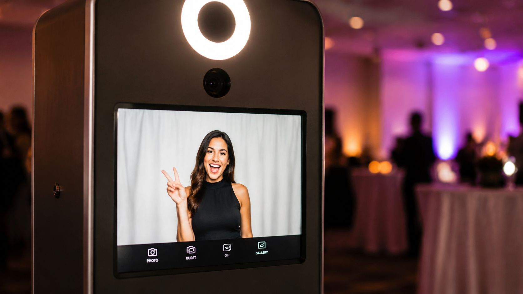 A sleek photo booth station with a touchscreen display featuring a woman posing with a peace sign.