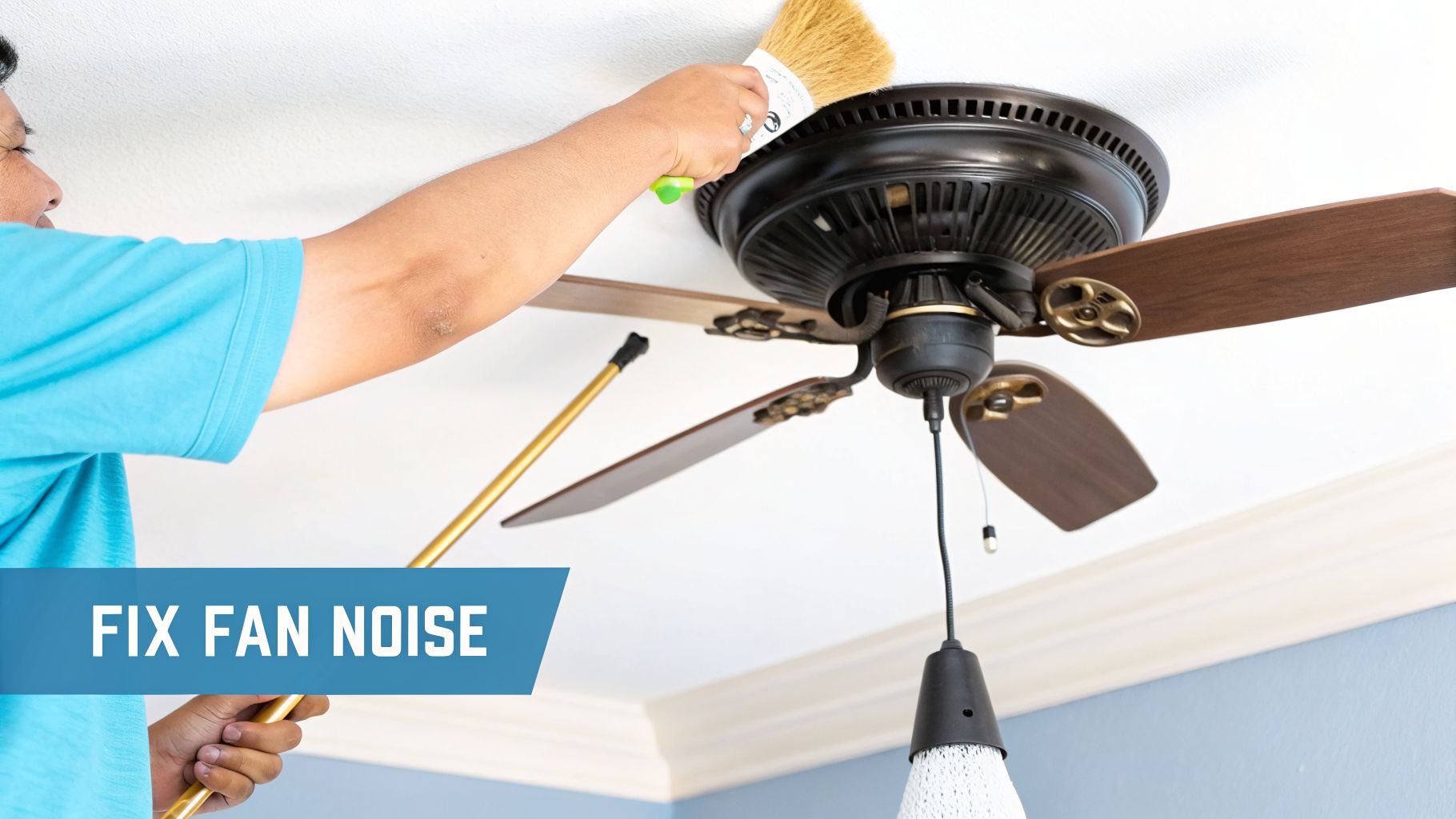 A person uses a brush to clean dust from the top of a dark ceiling fan, aimed at fixing fan noise.