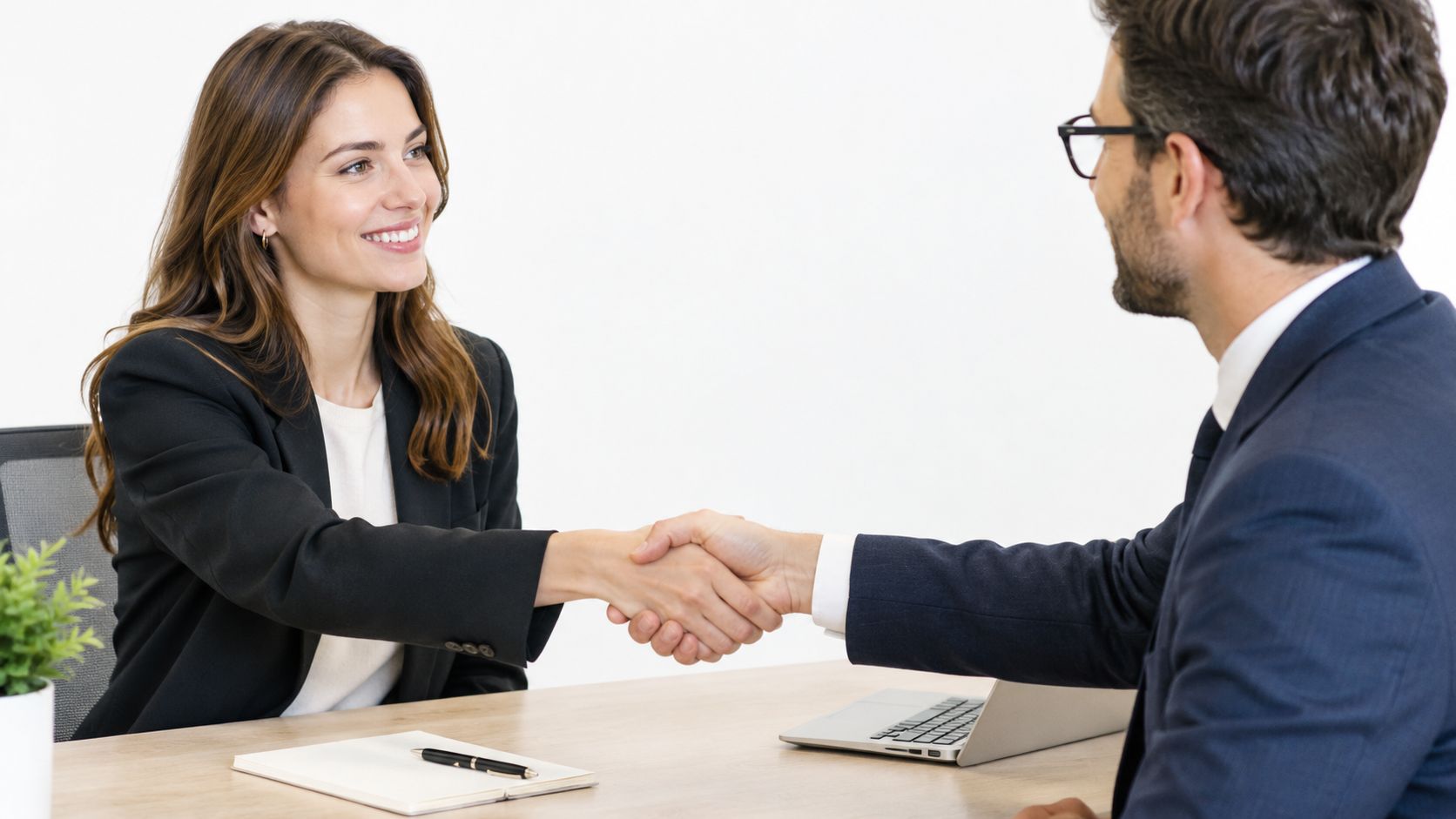 A job candidate and hiring manager shaking hands in an office, symbolizing the start of the interview stage.