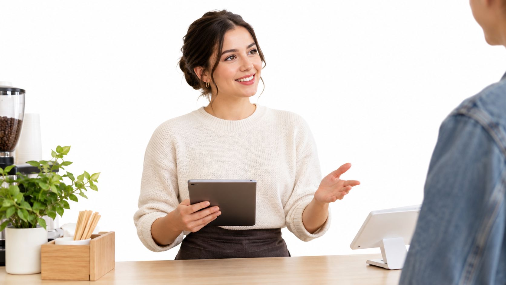 A friendly barista holding a tablet and smiling while greeting a customer at a cafe counter.