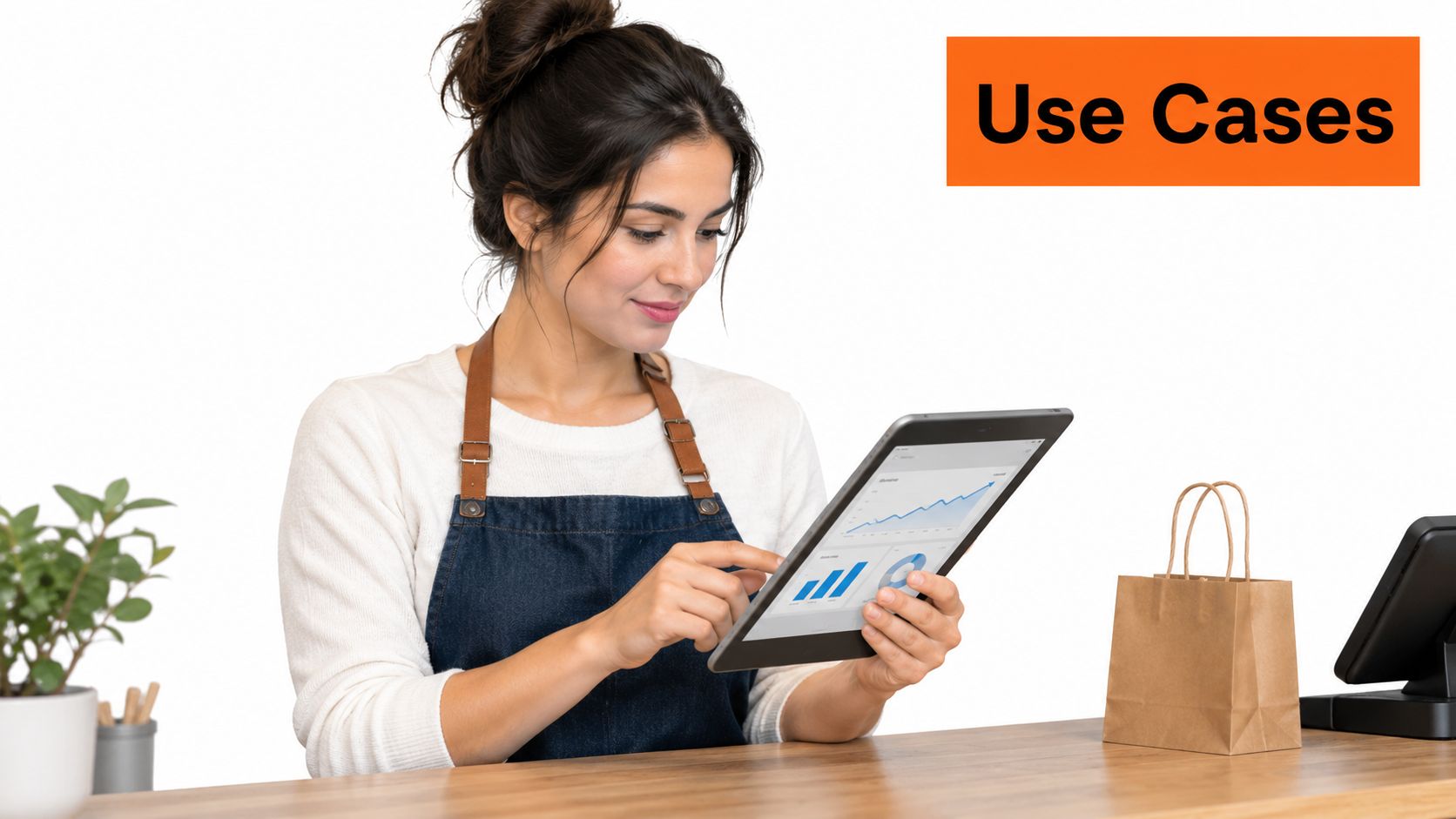 A female shop employee in an apron using a tablet to view business analytics at a counter.