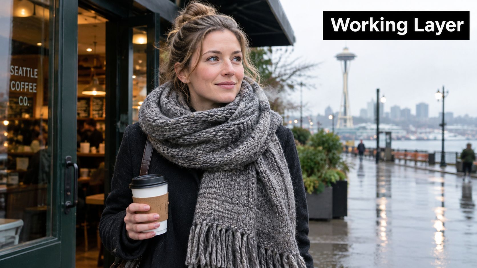 A smiling woman wearing a cozy gray knitted scarf holding a coffee cup by the Seattle waterfront.