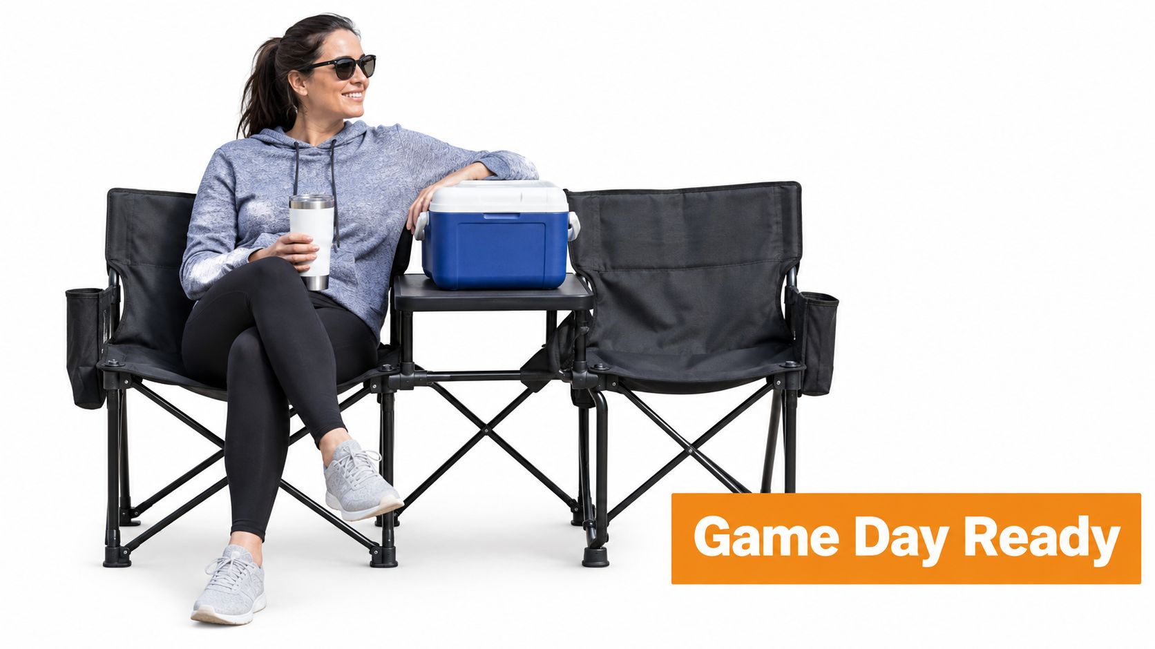 A smiling woman in a hoodie sitting on a two-seater folding chair with a built-in table and cooler.