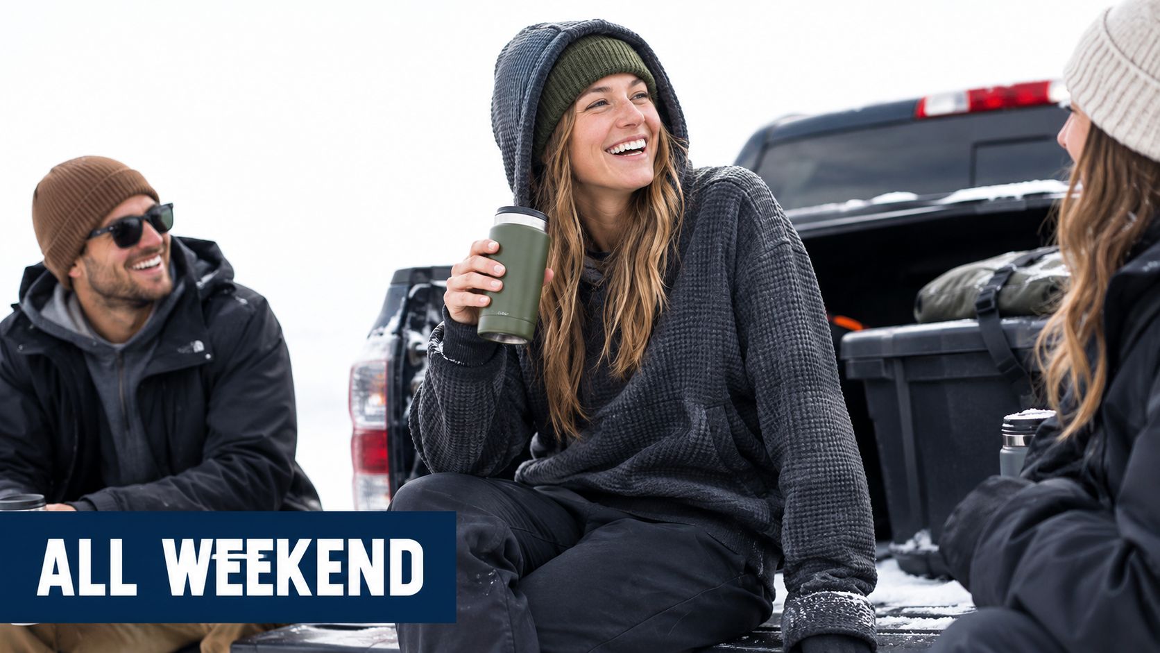 A cheerful group of three friends sitting on the back of a truck, wearing waffle knit hoodies.