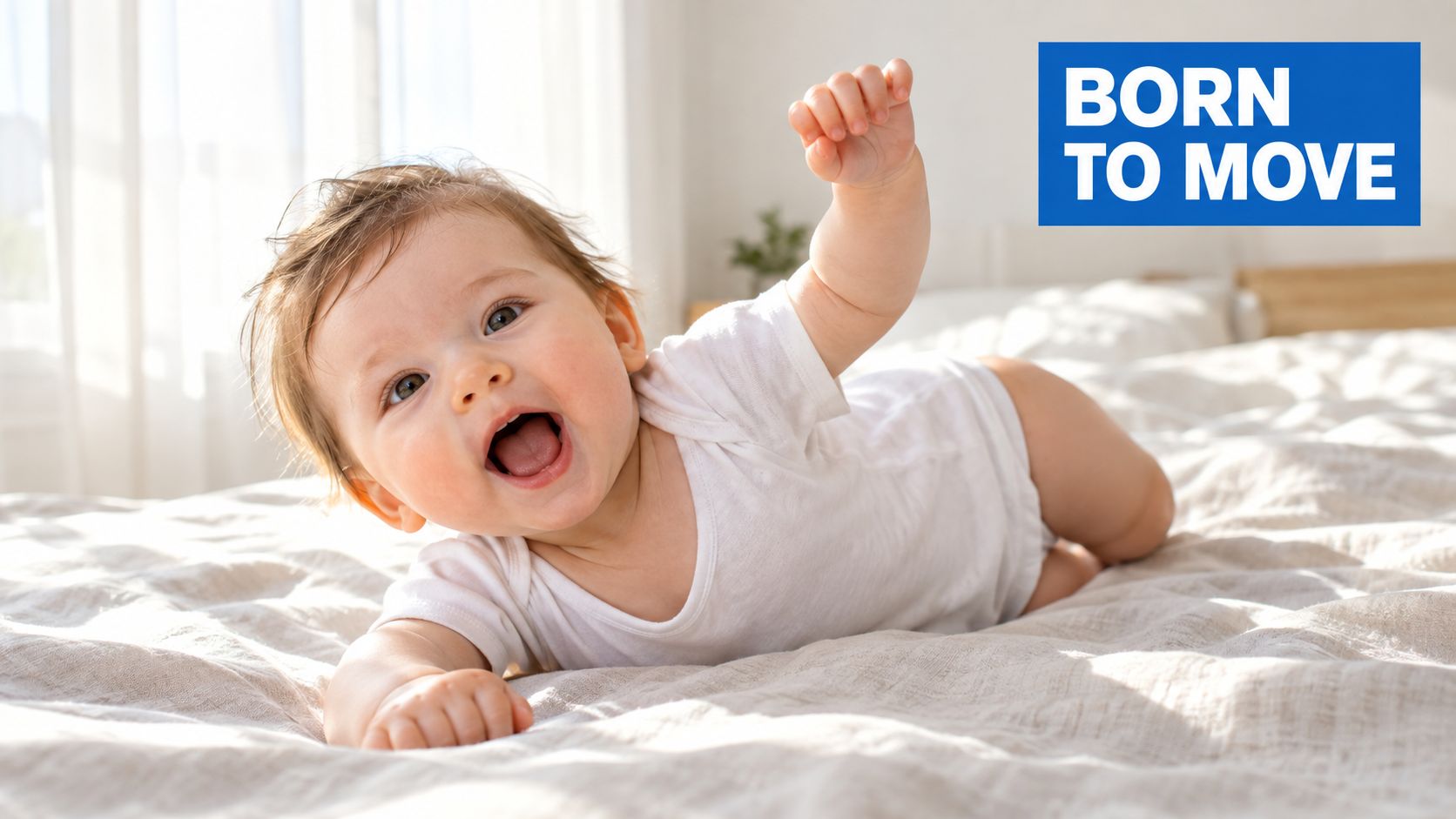 A joyful, active baby with messy hair lying on a soft bed, reaching up with one hand.