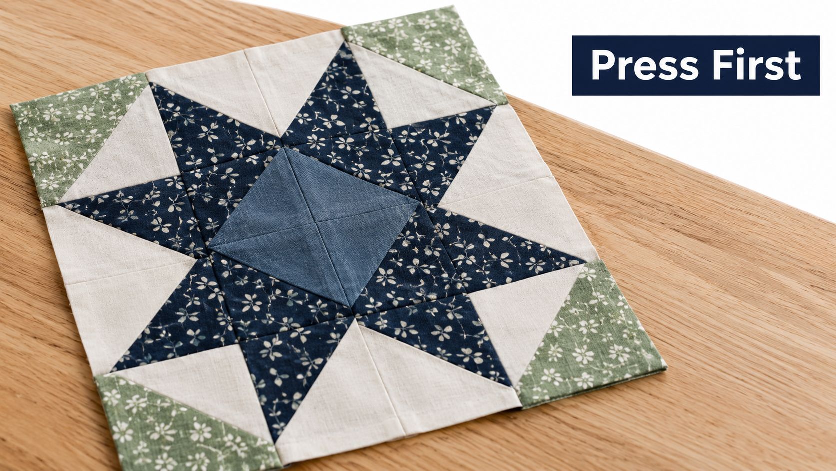 A square fabric quilt block featuring a blue and white star pattern resting on a wooden surface.