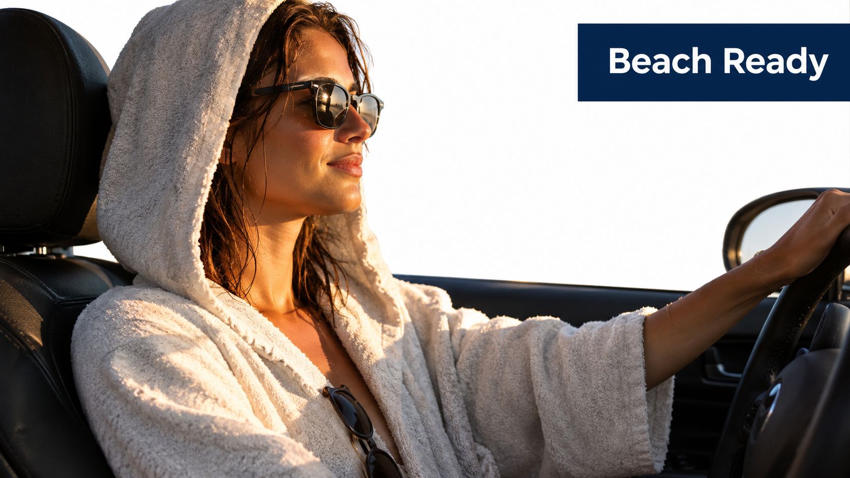 A woman wearing a white hooded robe driving a car during a sunny day at the beach.