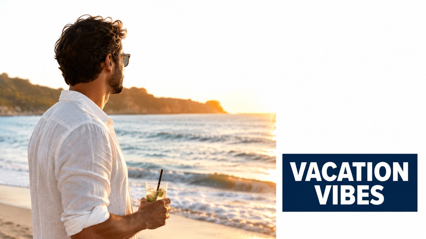 A man in a white linen shirt holding a cocktail while standing on a beach at sunset.