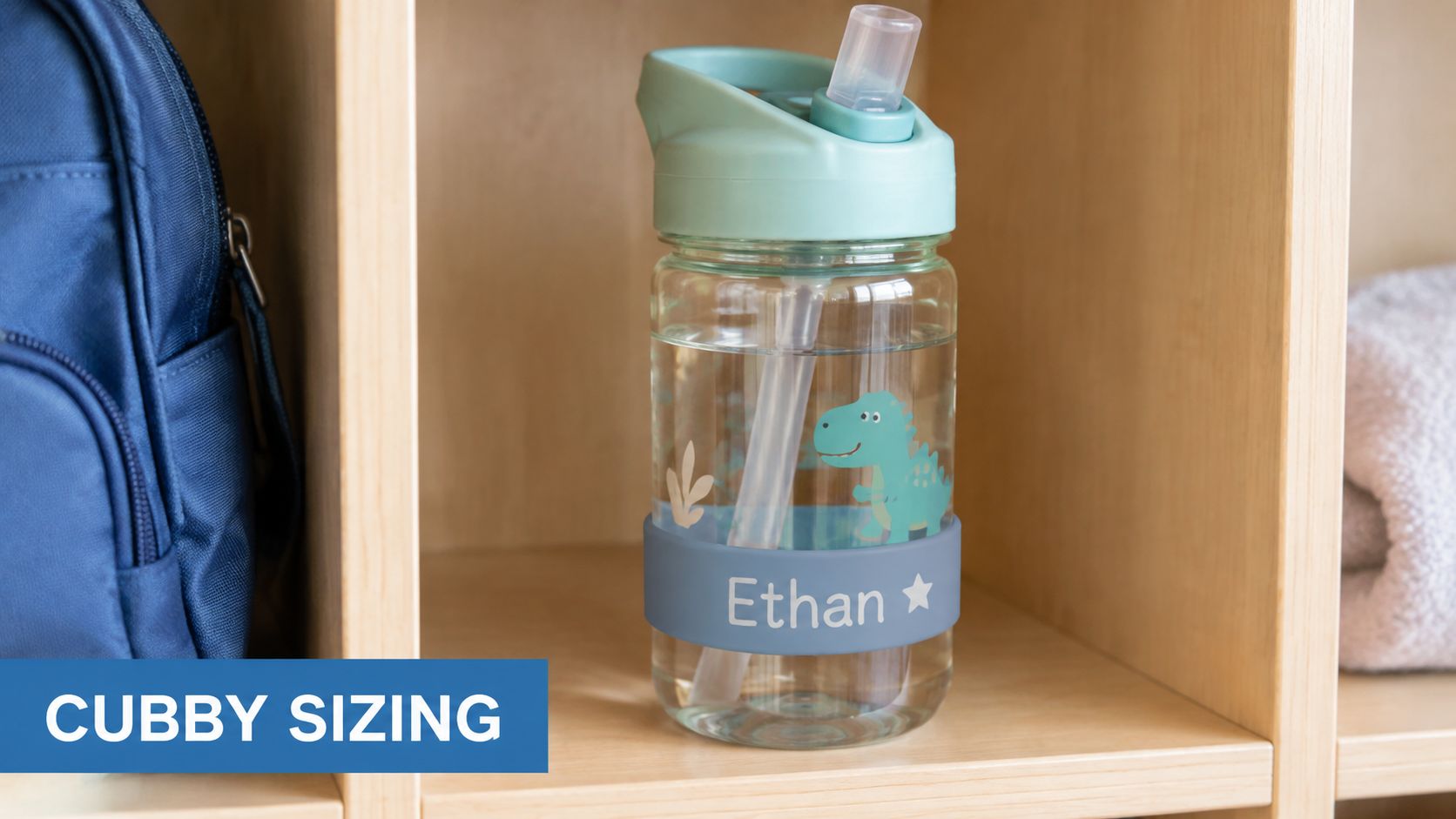 A clear water bottle with a dinosaur print and a custom Ethan name label in a cubby.