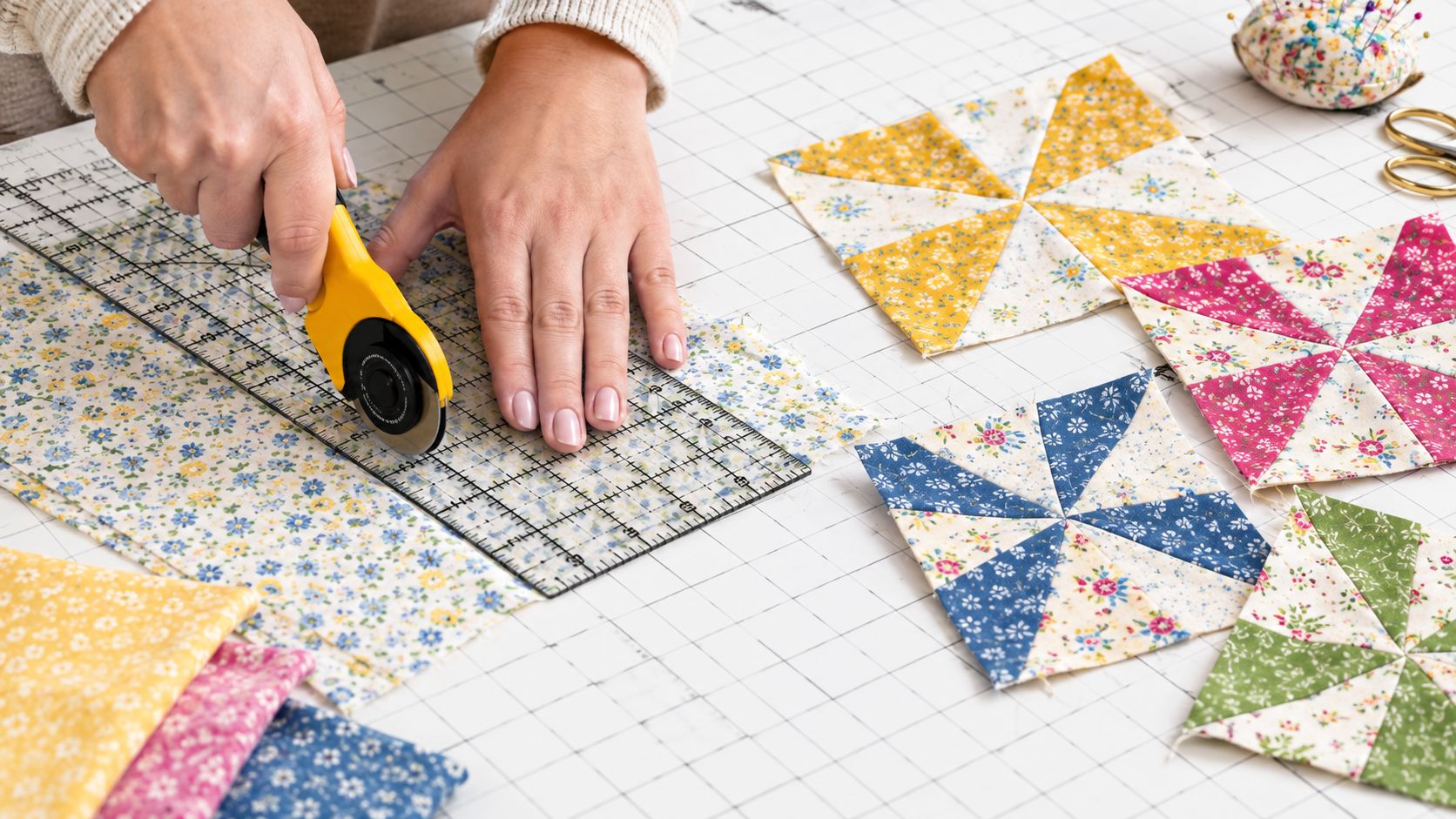 A quilter making an accurate cut in fabric using a rotary cutter and a special quilting ruler on a cutting mat.