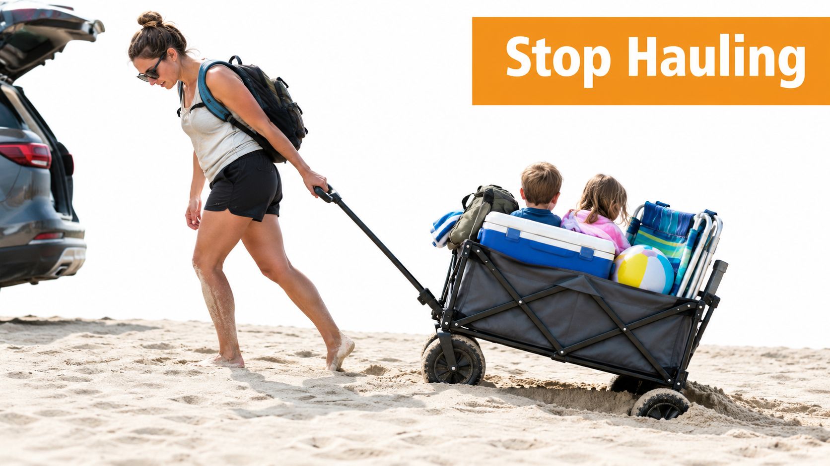 A woman pulls a folding wagon filled with children and beach gear across sandy beach terrain.