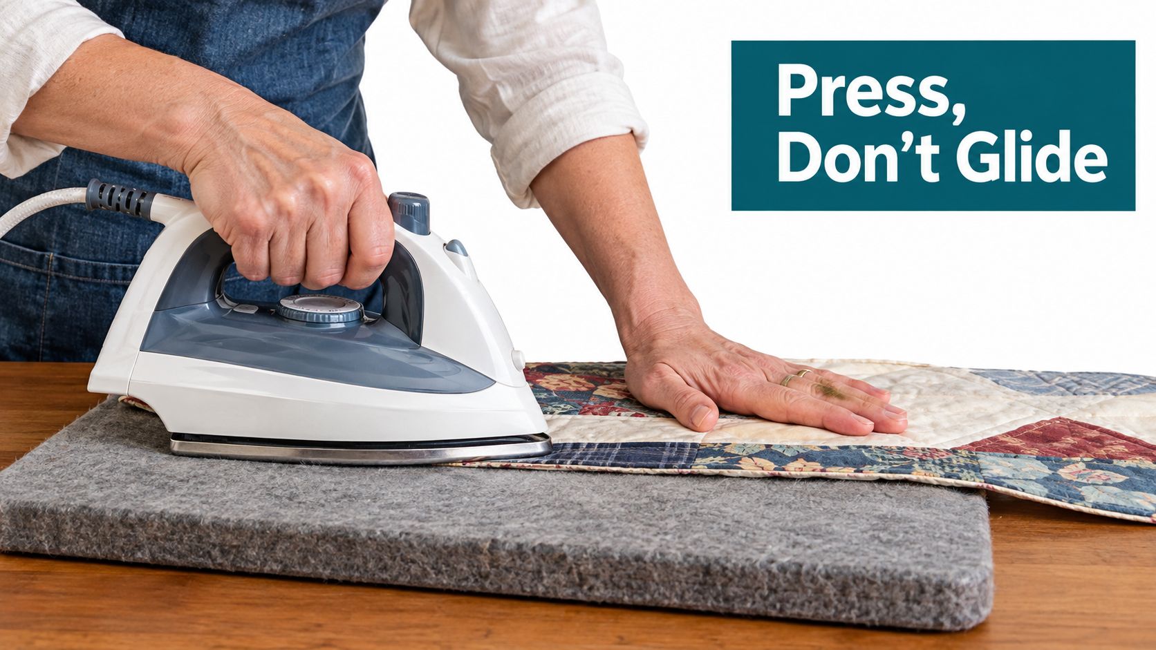 A person uses an iron to press a quilt on a grey wool pressing mat.