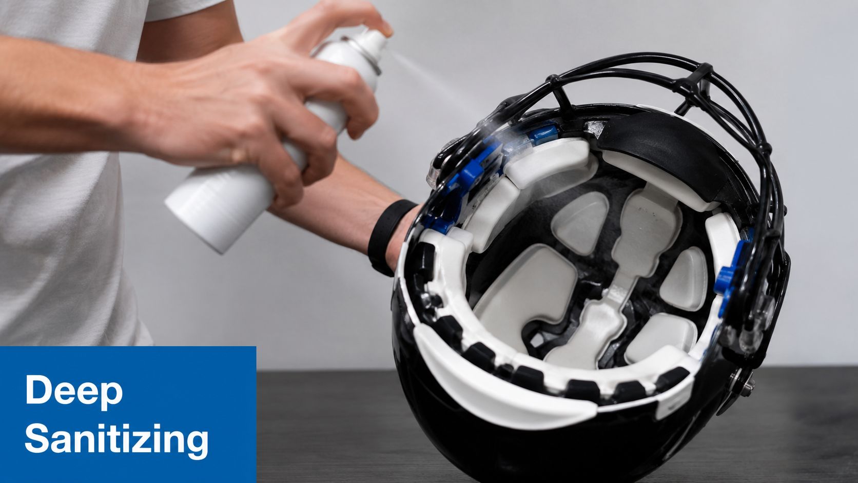 A person using a spray bottle to deep sanitize the inside of a black football helmet.