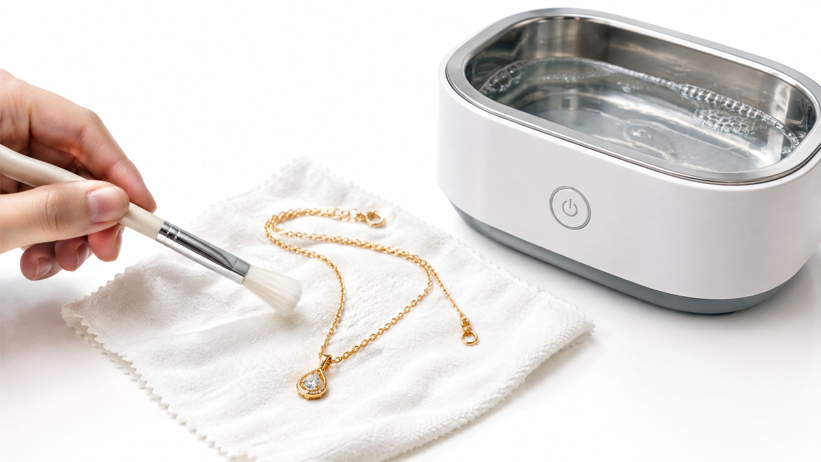 A hand using a small brush to clean a delicate gold necklace on a white cloth.