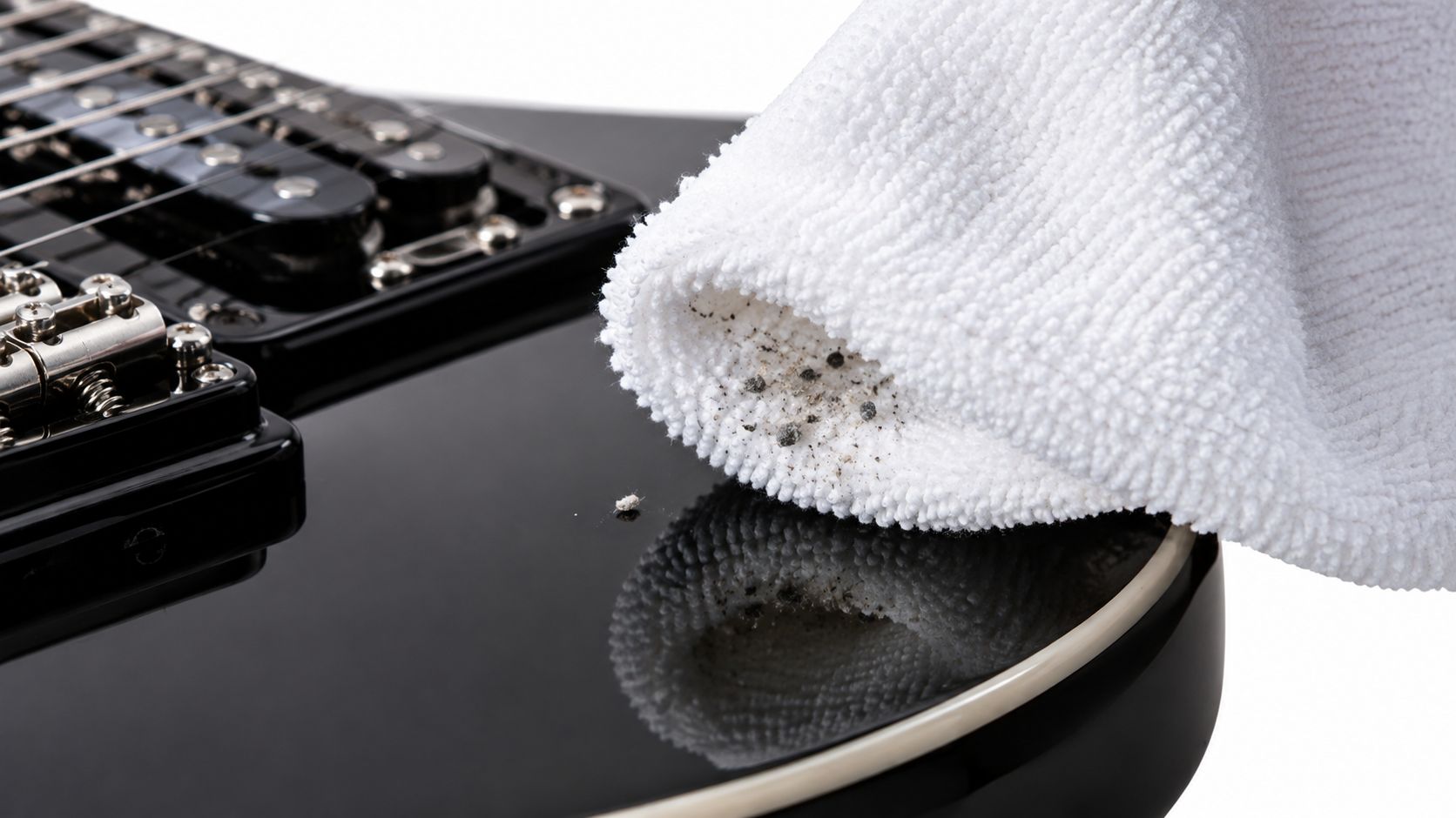 A close-up view of a white microfiber cloth cleaning dust off a glossy black electric guitar.