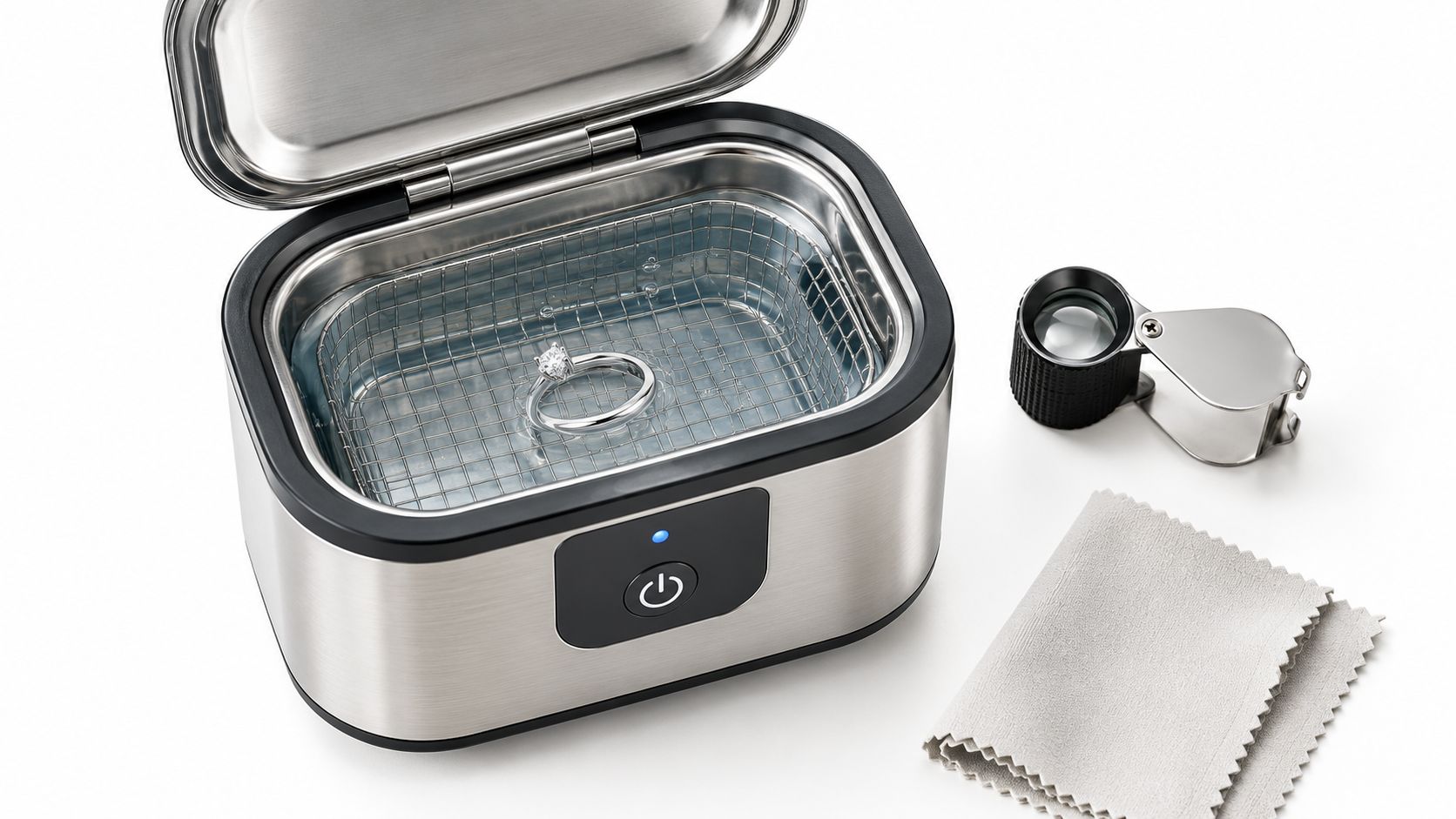 A stainless steel ultrasonic jewelry cleaner containing a white gold diamond ring next to a loupe and cloth.