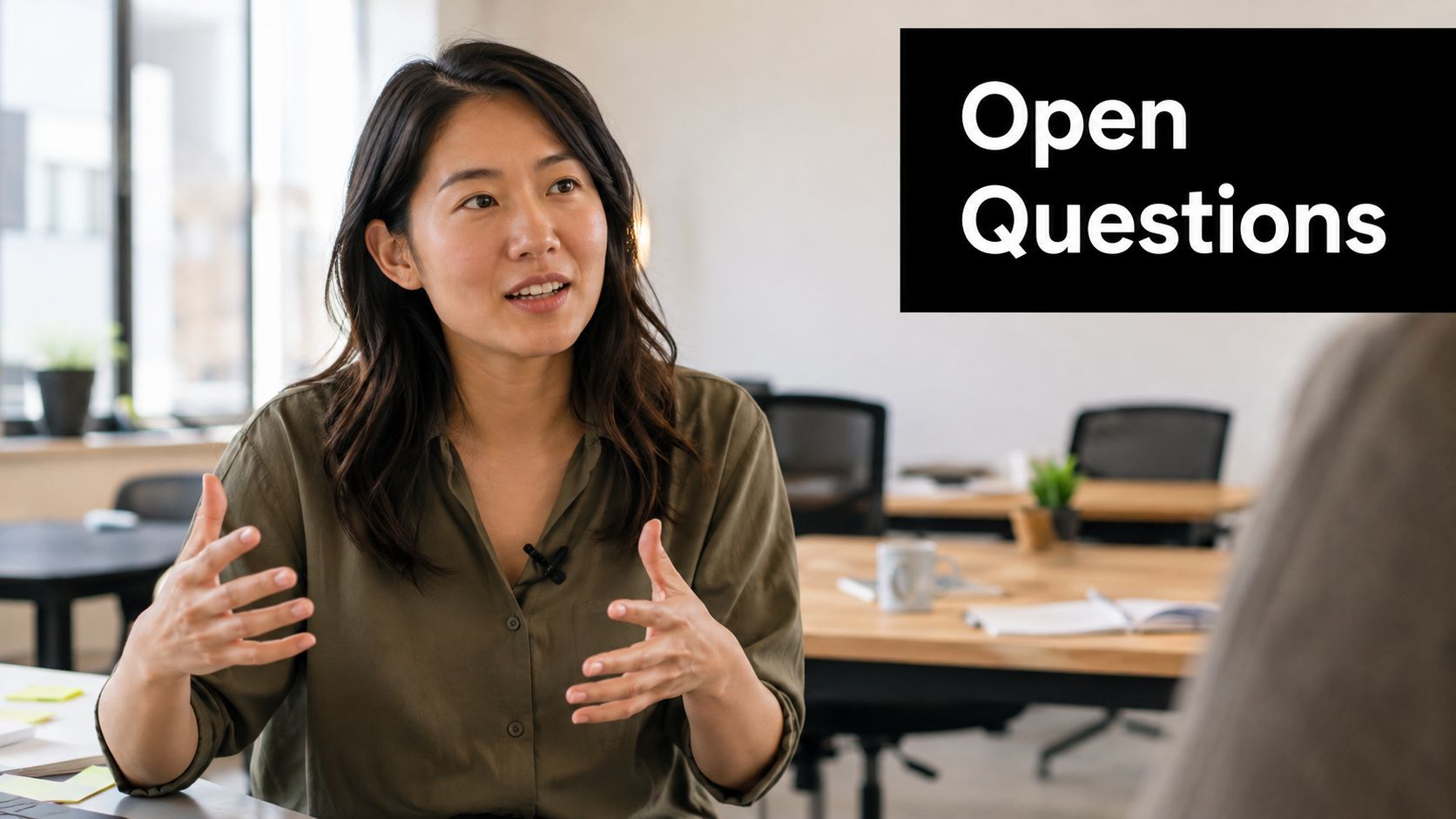 A professional woman sitting in an office environment gesturing while having a conversation about open questions.