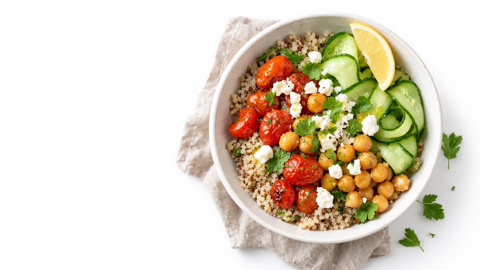A healthy quinoa salad bowl topped with roasted tomatoes, chickpeas, cucumber ribbons, feta cheese, and fresh parsley.