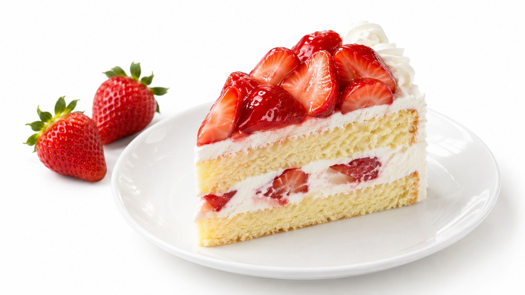 A delicious slice of strawberry shortcake with fresh cream on a white plate with whole strawberries.
