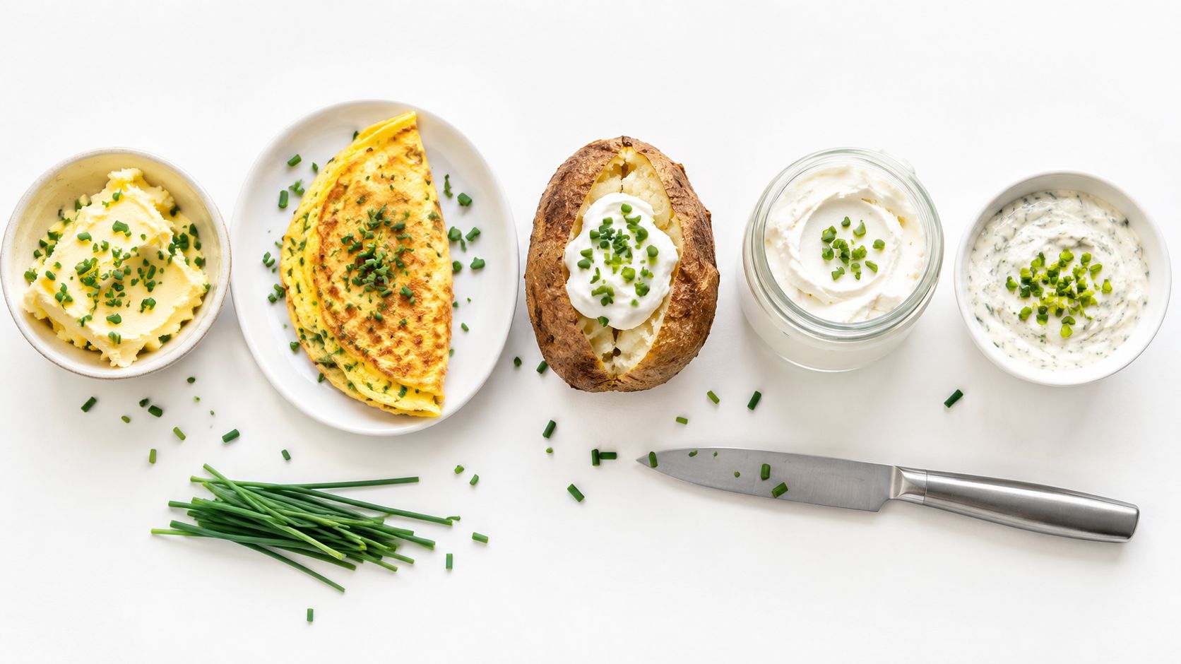 An overhead view of a delicious omelet, baked potato, butter, cream cheese, and fresh chives.