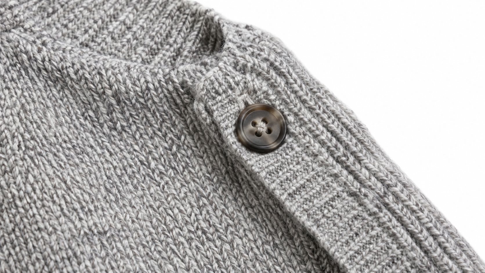 Close-up of a light grey knitted wool sweater featuring a detailed button detail on the shoulder.