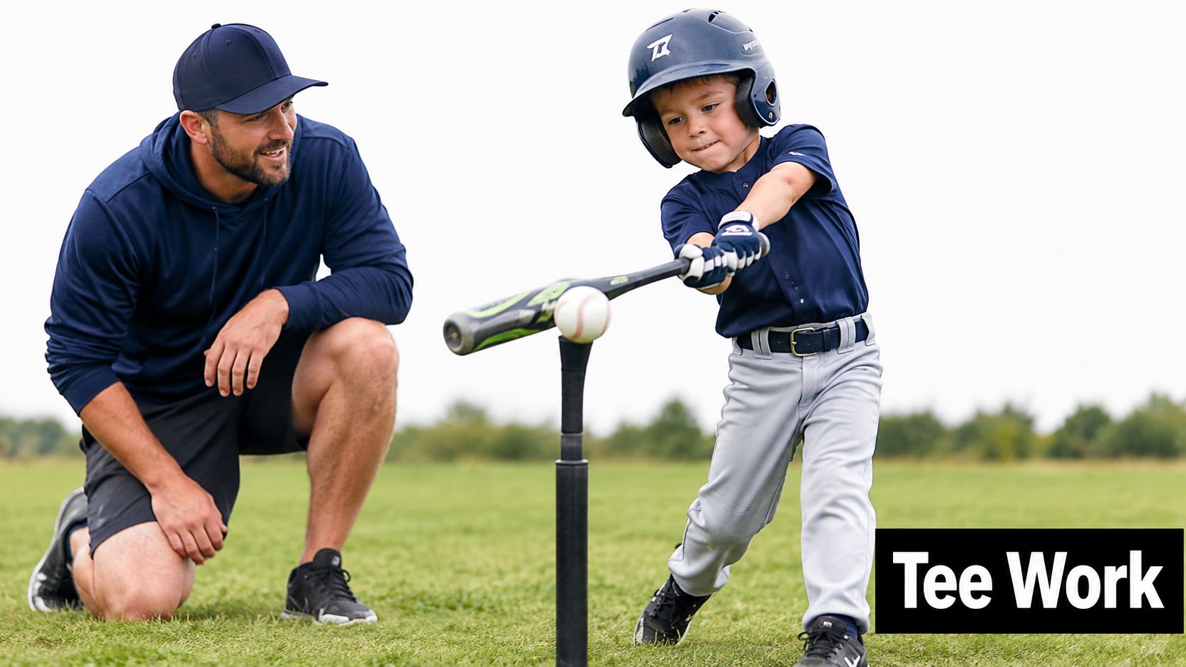 A father kneeling on the grass watching his young son practice hitting a baseball off a tee.