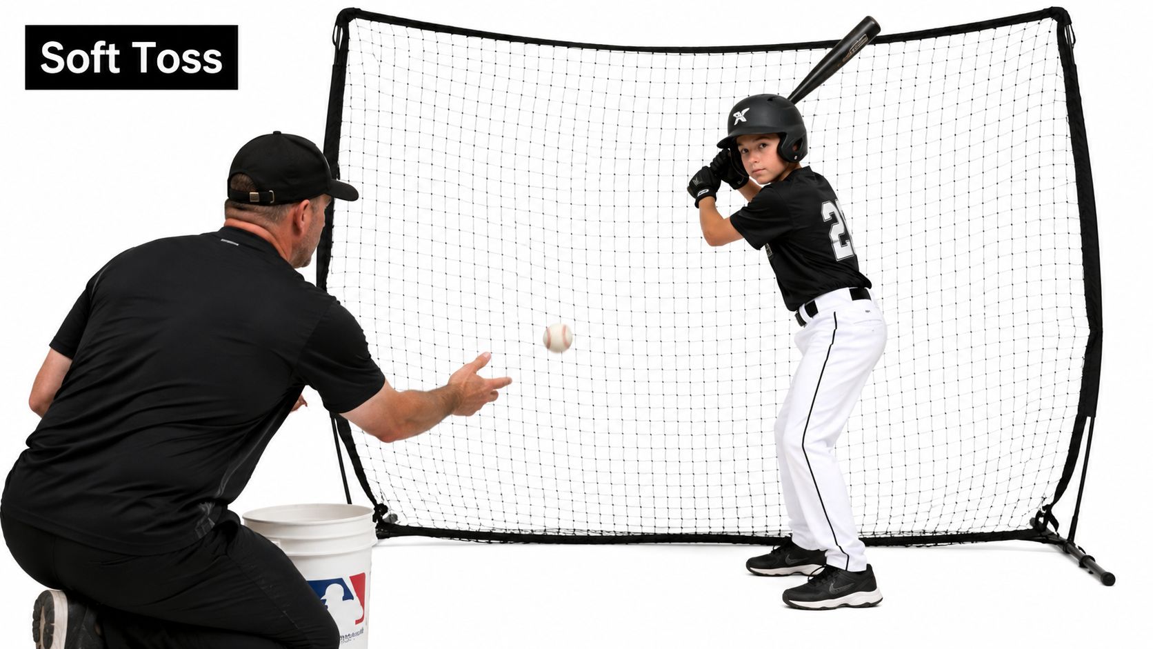 A coach tosses a baseball to a young batter wearing a helmet, training with a hitting net.