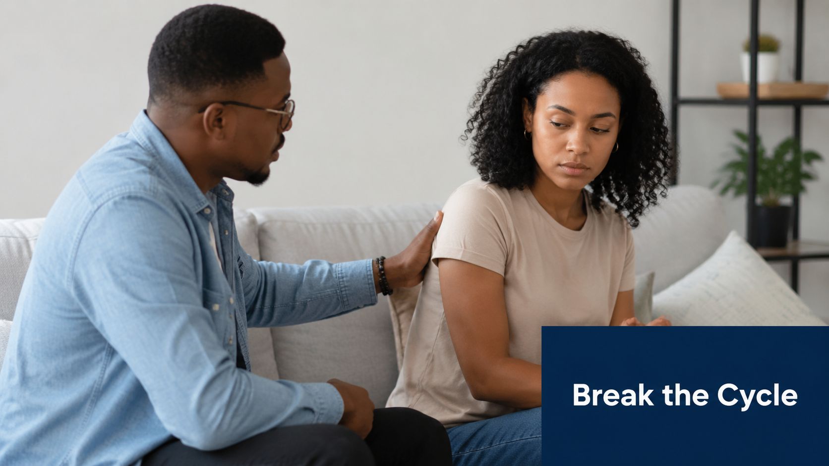 A concerned man reaches out to comfort a sad woman sitting on a light-colored couch together.