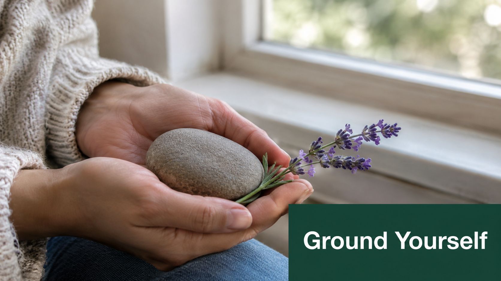 A person holding a smooth gray river stone and a sprig of fresh lavender in their hands.