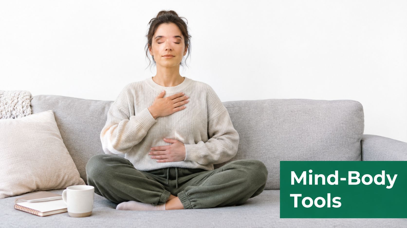 A woman meditating on a sofa with her hands on her chest and abdomen for mindful breathing.