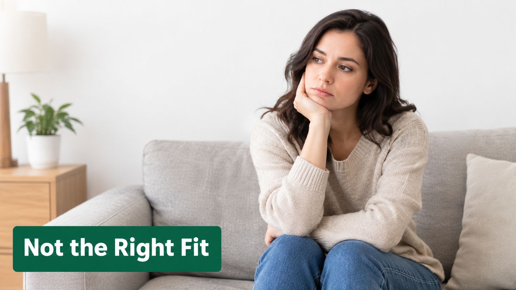 A pensive woman sits on a grey couch, reflecting on a poor therapy fit experience.