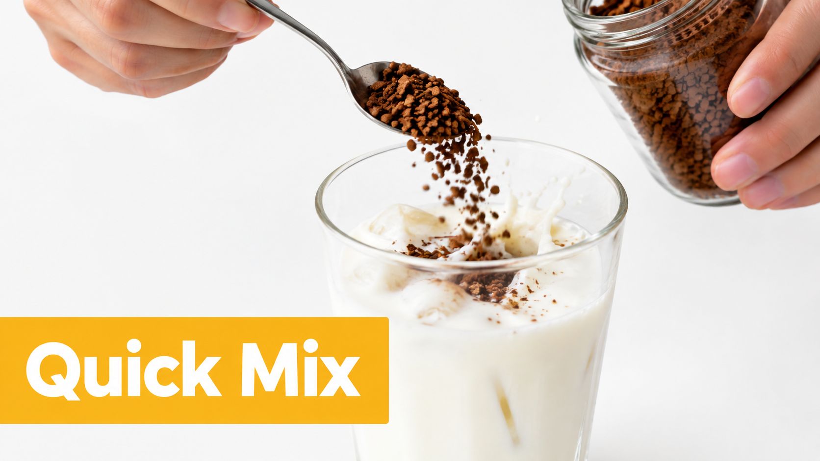 A person pouring instant coffee granules from a spoon into a glass of milk with ice.