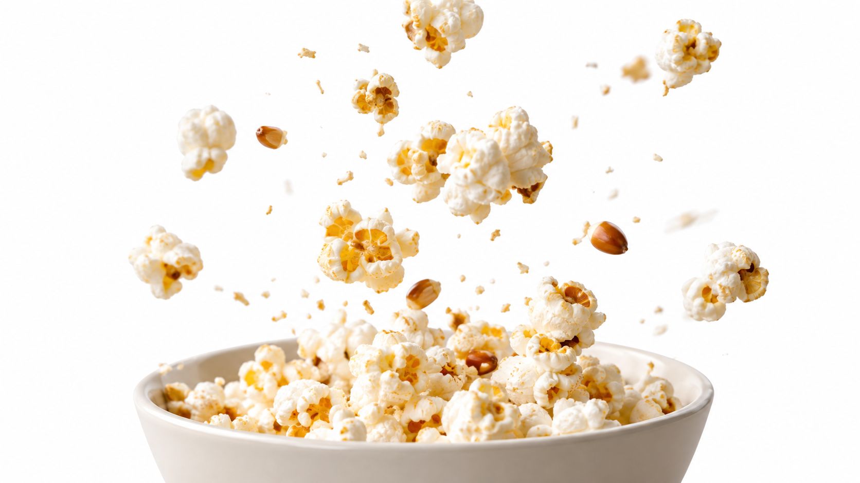 A close-up shot of popcorn kernels popping and exploding out of a white ceramic bowl.