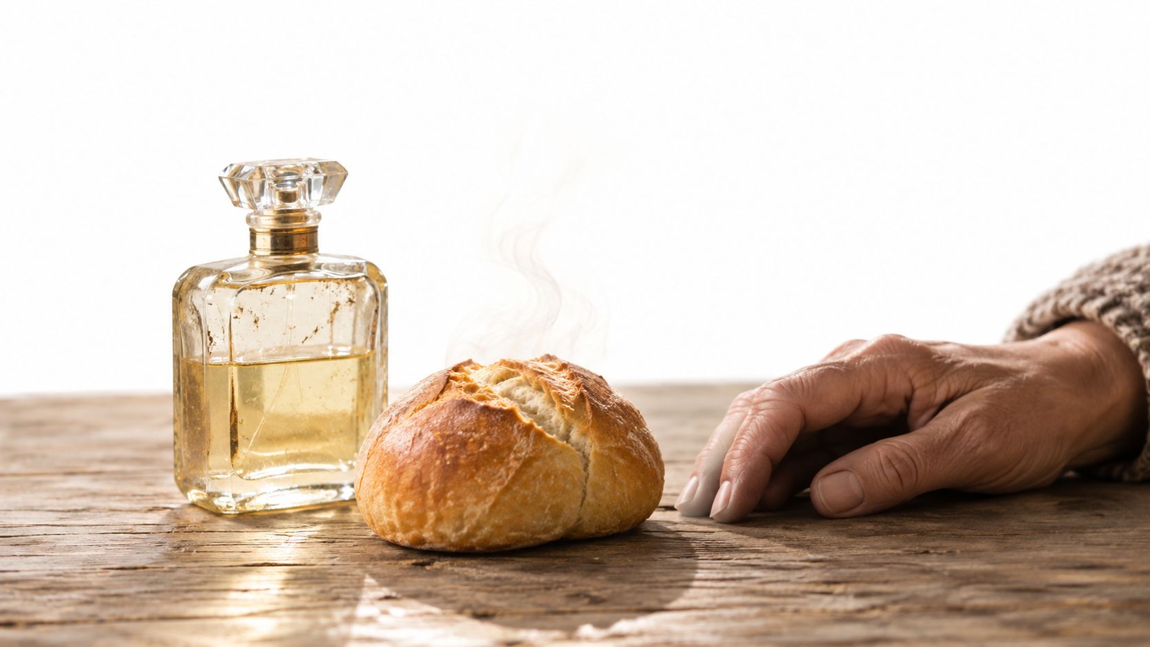 A close-up of a loaf of steaming bread next to a perfume bottle and a person's hand.